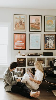 a man and woman sitting on the floor in front of a book shelf with books