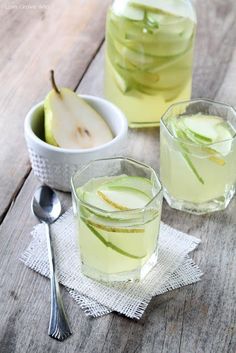 two glasses filled with apple cider sitting on top of a wooden table next to silverware