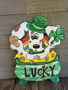 a wooden sign that says lucky with a dog wearing a hat and holding a shamrock