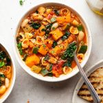 three bowls filled with pasta and vegetables on top of a white table next to bread