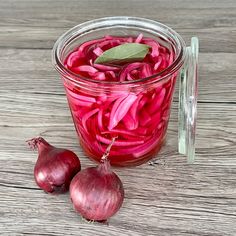 red onions are in a glass jar on a wooden table next to two garlic cloves