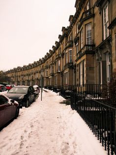 cars parked on the side of a snow covered street in front of row houses with black iron railings