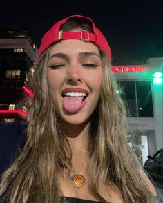 a woman sticking her tongue out in front of a building at night with bright lights