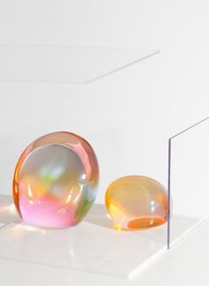 two glass balls sitting on top of a white surface next to a square piece of metal