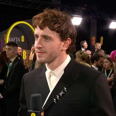 a man in a tuxedo is talking to the camera at an awards event