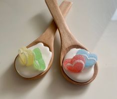 two wooden spoons with different colored candies in them on a white counter top