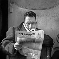 a man sitting at a table reading a newspaper while holding his head in his hands