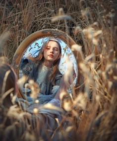 a woman sitting in tall grass looking into a mirror