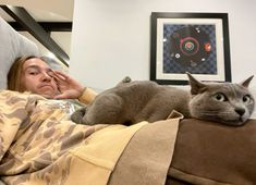 a woman laying on top of a bed next to a gray and white cat with green eyes