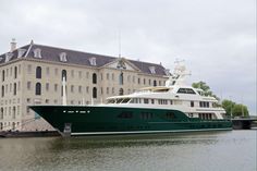 a large green and white boat in front of a big building on the water near some docks