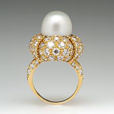 This magnificent cocktail ring is centered with one (1), post set, cultured South Sea pearl. The pearl tops a domed setting is bead set sixty-four (64), bead set, round brilliant cut diamonds. The ring has a split shank design and is accented with seven (7), bead set, round brilliant cut diamonds on each side. The ring measures 21.7mm at the top, rises 18.6mm above the finger, tapering to 2.4mm wide and 1.1mm thick at the base of the shank. The ring is currently size 7. Elegant White Domed Rings, Elegant White Domed Jewelry, White Pearl Ring With 17 Jewels For Formal Occasions, Elegant Domed White Gold Jewelry, Classic Cabochon Pearl Ring For Formal Occasions, Classic Formal Pearl Ring With Cabochon, Elegant Diamond White Dome Ring For Formal Occasions, Elegant Dome Ring With Cabochon For Wedding, Elegant Dome Diamond Ring