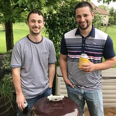 two men standing next to each other in front of a bbq with a drink