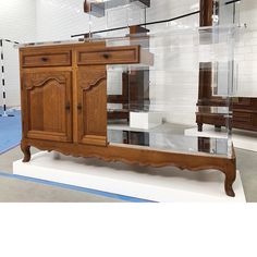 a wooden cabinet with glass doors and drawers on display in a room filled with white tile walls