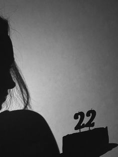 a woman holding a cake with the number 22 on it in front of a white wall