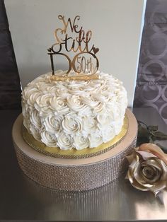 a cake with white frosting and gold trimmings sits on a table next to a rose