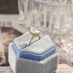 an engagement ring sits on top of a blue velvet box in front of some wine glasses