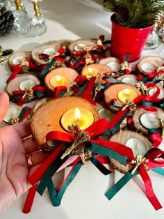 a person holding a lit candle in front of some christmas decorations on a table with pine cones