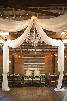 the inside of a barn decorated with white draping and chandelier hanging from the ceiling