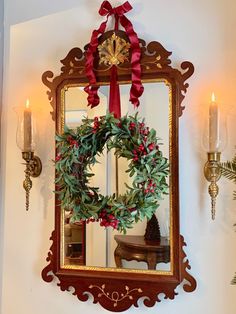 a mirror hanging on the wall with a wreath in front of it and two candles