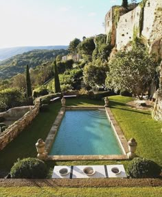 an outdoor swimming pool surrounded by greenery and stone walls with trees in the background