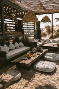 an outdoor living area with couches and pillows on the sand under a pergolated roof