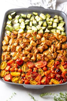 a pan filled with chicken, tomatoes and cucumbers on top of a table