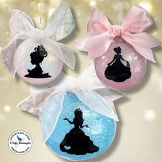 three ornaments with the silhouettes of disney princesses on them are hanging from ribbons