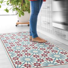 a woman standing on the kitchen floor in front of an oven and potted plant