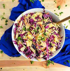 a white bowl filled with coleslaw and apples on top of a wooden table