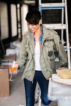 a woman holding a wine glass while standing on a steplader in an unfinished building