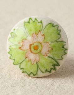 a green and white ceramic object with flowers painted on it's side, sitting on the ground