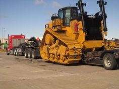 a large yellow bulldozer sitting on the back of a semi truck in a parking lot