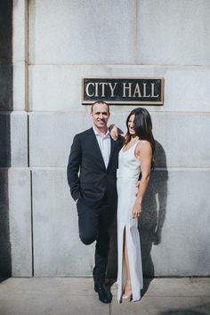 a man and woman standing in front of a city hall sign