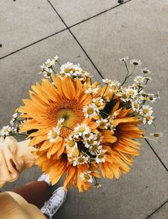 a person holding a bouquet of sunflowers and daisies in their hand on the sidewalk