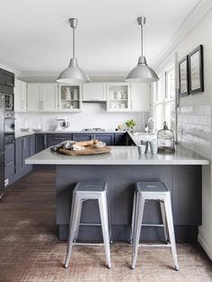 two stools are in front of the kitchen island and countertop, which is surrounded by gray cabinets