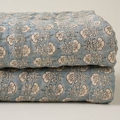 two blue bedspreads with white flowers on them, one is rolled up and the other has been folded down