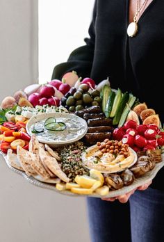 a woman holding a platter filled with different types of food and dips on it