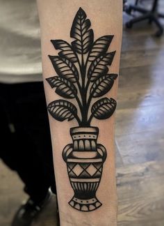 a black and white vase with leaves on the arm, done by tattoo artist person