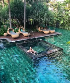 a man sitting in the middle of a pool surrounded by lounge chairs and palm trees