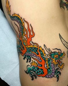 a colorful dragon tattoo on the side of a woman's stomach, with an orange flame coming out of it