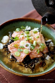 someone is pouring sauce on some food in a green bowl with rice and other ingredients