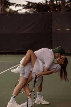 two people on a tennis court with rackets in their hands and one holding the other's leg