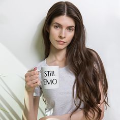 a woman holding a coffee mug with the word still emo on it