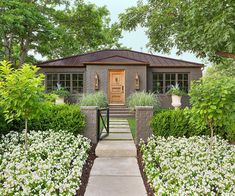 a house that is surrounded by white flowers and greenery, with a wooden door