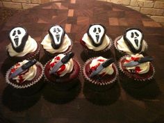 six cupcakes with white frosting and black icing decorated as ghost faces