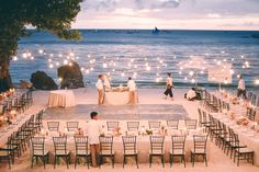 an outdoor dinner setup on the beach with people standing around and looking out at the water