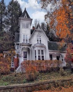 a large white house sitting on top of a lush green hillside next to fall trees