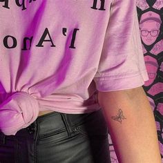 a woman wearing a pink shirt and black leather pants with tattoos on her left arm