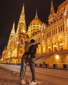 two people standing in front of a building at night with their arms around each other