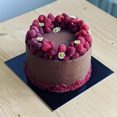 a chocolate cake with raspberries and daisies on top sitting on a wooden table